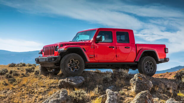 A red Jeep Gladiator parked on rocky terrain under a bright blue sky