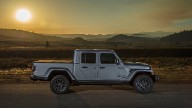 A silver Jeep Gladiator parked on a road with hills and sunset in the background