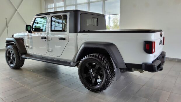 A white Jeep Gladiator with black wheels parked inside a showroom with large windows