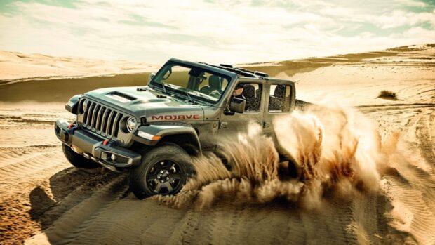 Jeep Gladiator driving through the sand dunes in a desert with dust flying around