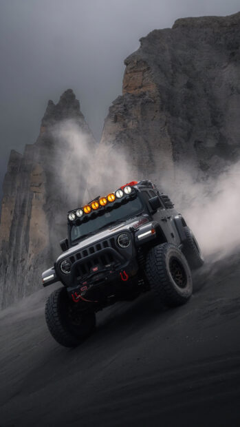 Black Jeep Gladiator driving on dusty terrain near rocky cliffs at dusk