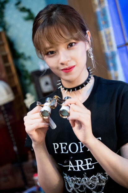 Jeongyeon Twice holding vintage binoculars inside a cozy room with a smile, 2K Mobile Wallpaper