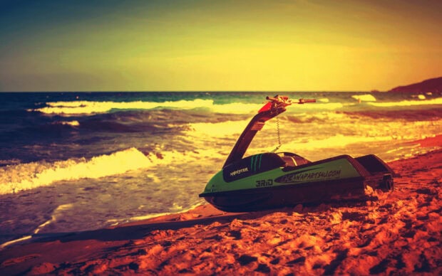 A jet ski rests on the sandy beach with waves crashing nearby under a bright sky, 2K Desktop Wallpaper
