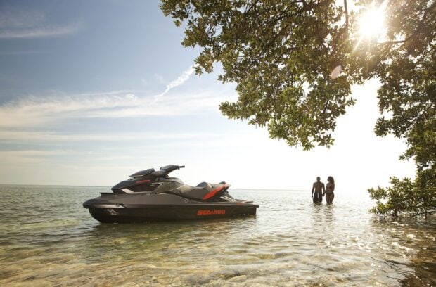 A jet ski rests near shore with two people standing in shallow water under a sunny sky, HD Desktop Wallpaper