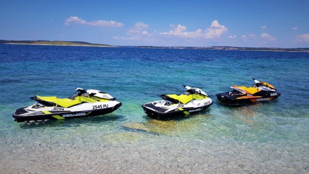 Three jet skis are parked on the transparent shallow water near the shore, HD Desktop Wallpaper