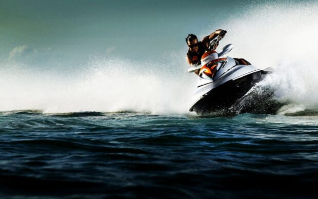 A jet ski rider is making sharp turns on the ocean surface under clear skies, HD Desktop Wallpaper