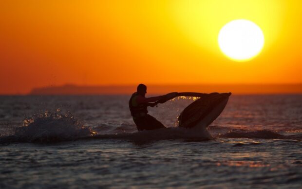 A person riding a jet ski on the water during a vibrant orange sunset, HD Desktop Wallpaper
