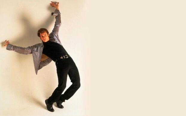 Jim Carrey is posing with a dramatic lean against a plain beige background, HD Desktop Wallpaper