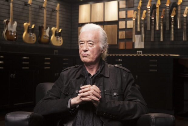 Jimmy Page sitting thoughtfully in a guitar workshop surrounded by electric guitars