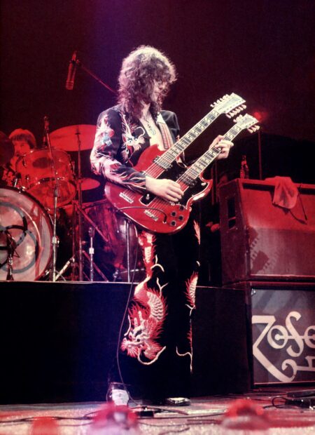 Jimmy Page playing a double neck guitar on stage wearing embroidered pants and jacket