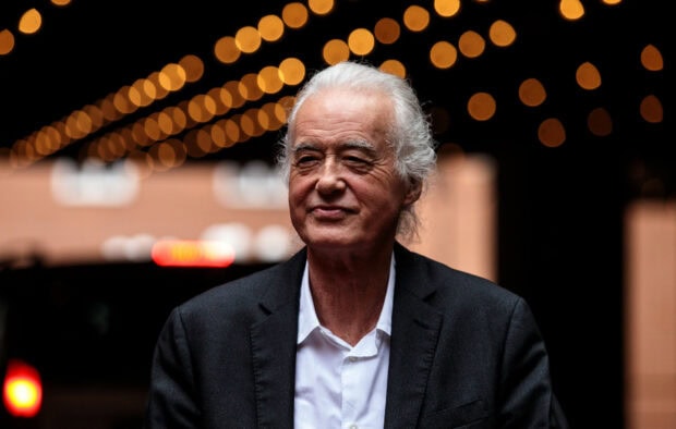 Jimmy Page wearing a black suit and white shirt with festive lights in the background