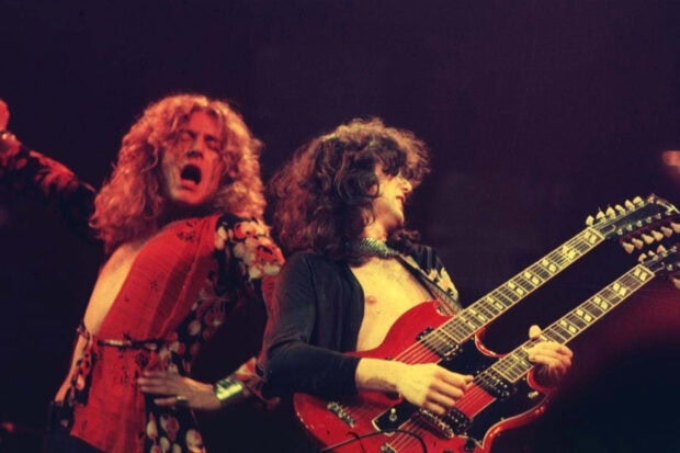 Jimmy Page playing double neck guitar on stage with singer performing nearby
