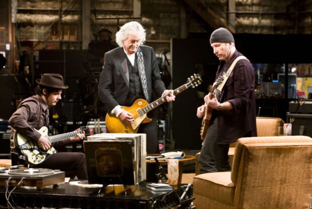Jimmy Page playing guitar with two other musicians in a cozy studio setting
