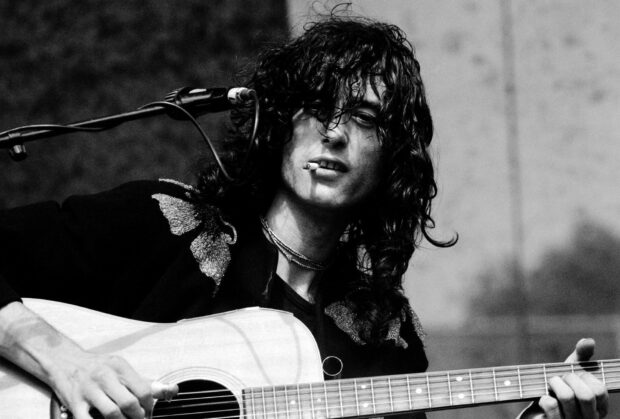 Jimmy Page playing acoustic guitar with a cigarette in his mouth during a live performance