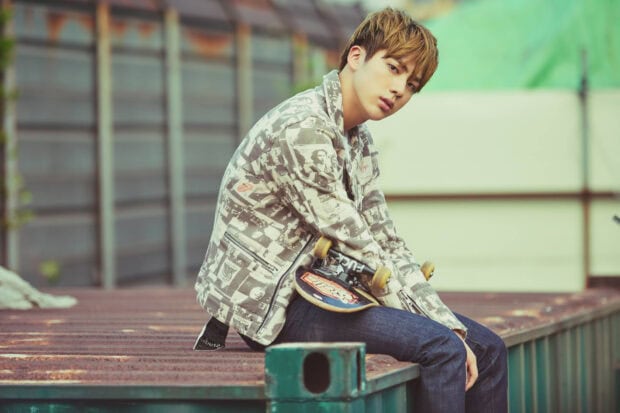 A young man wearing a patterned jacket holds a skateboard while sitting outdoors, HD Desktop Wallpaper