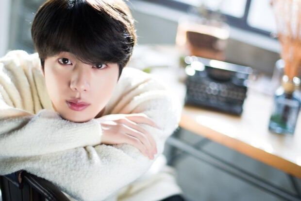 Jin Bts is sitting with arms crossed in front of a desk in a bright room, HD Desktop Wallpaper