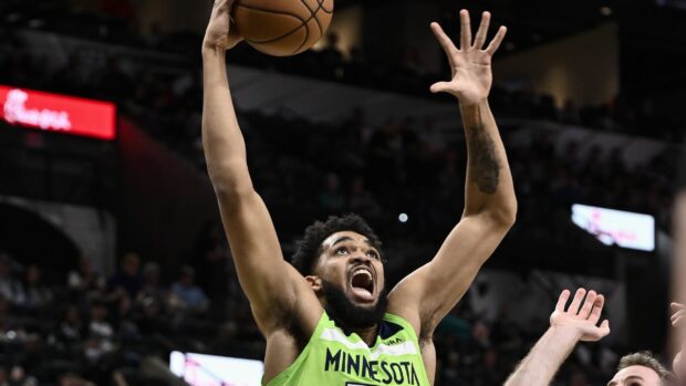 Karl Anthony Towns in a Minnesota basketball jersey reaching up to score during a game in an arena
