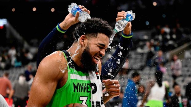 Karl Anthony Towns smiling as a basketball player gets water poured on his head on court