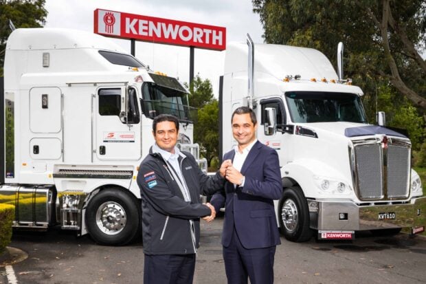 Two men shaking hands in front of Kenworth trucks at a dealership, 2K Desktop Wallpaper