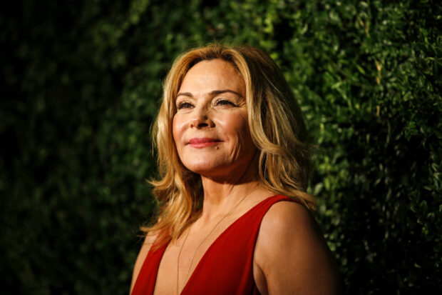 Kim Cattrall wears a red dress while standing in front of green foliage, HD Desktop Wallpaper