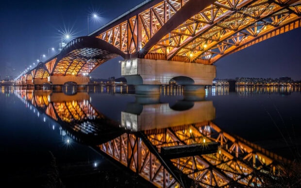 A night view of Korea bridge structure reflecting on calm water with city lights in the background