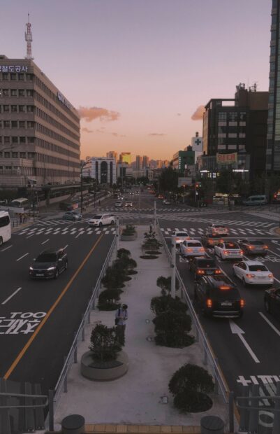 A busy street scene in Korea with cars and a pedestrian under a sunset sky