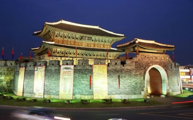 Night view of a traditional Korea fortress with illuminated walls and historical banners