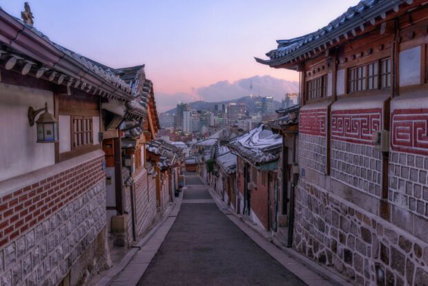Traditional Korean street with hanok houses and Seoul cityscape in the background at sunset