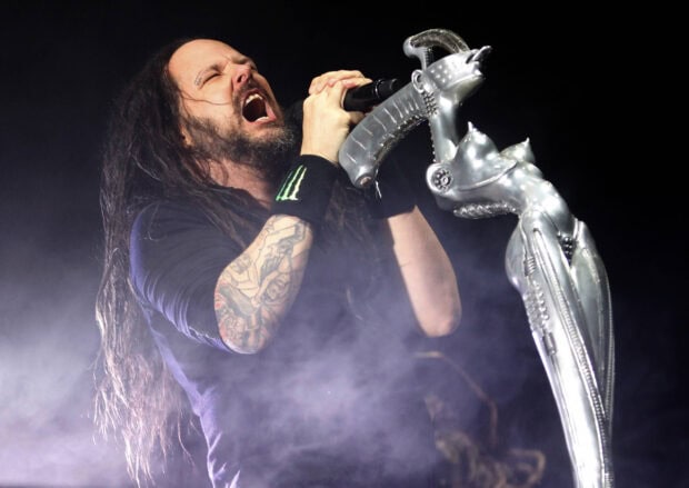 Korn performing live on stage with a microphone stand in a smoke filled environment