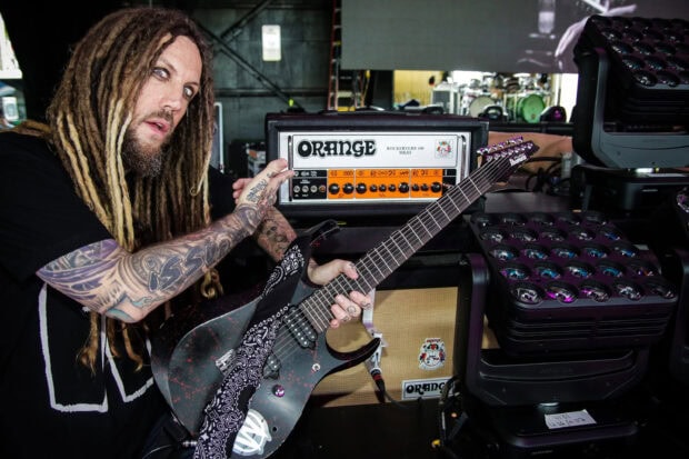 Tattooed guitarist from Korn holding an electric guitar near Orange amplifier gear