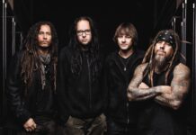 The Korn band members posing together with long hair and tattoos in a dark setting