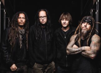 The Korn band members posing together with long hair and tattoos in a dark setting
