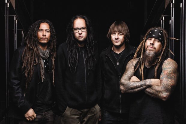 The Korn band members posing together with long hair and tattoos in a dark setting