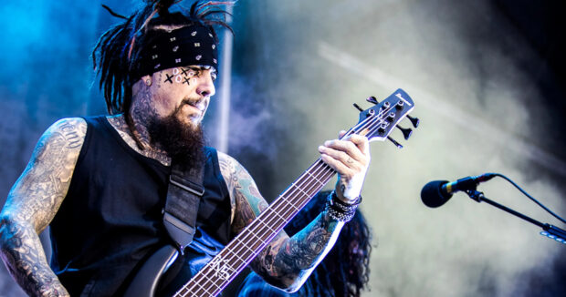 Korn band member playing bass guitar on stage with visible tattoos and face paint