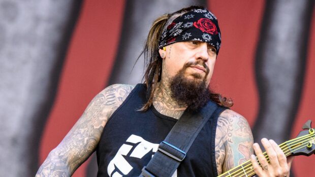Korn musician playing bass guitar with tattoos and a bandana on stage