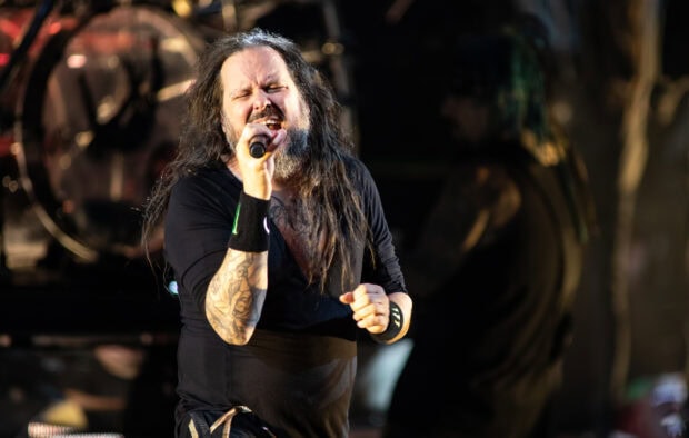 Korn vocalist performing live on stage with passion and tattoos visible on his arm