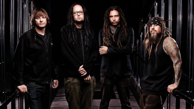 The Korn band members stand together in a dark setting with serious expressions and casual clothing