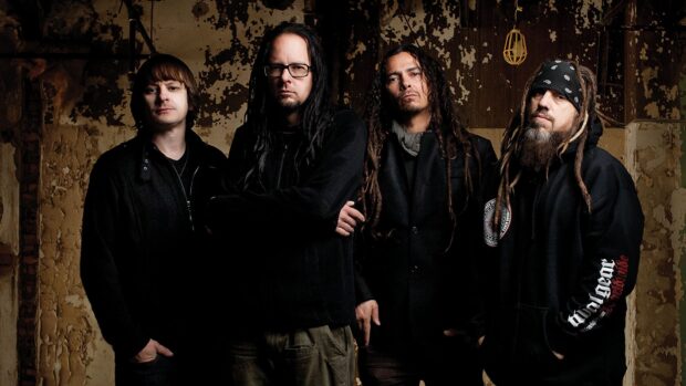 The Korn band members standing together in a rustic setting with worn walls in the background
