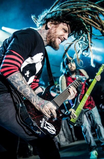 A Korn musician playing guitar passionately during a live concert with dreadlocks flying in the air