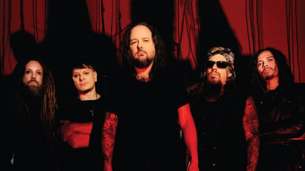 Korn band members standing against a red backdrop with dark shadows and intense expressions