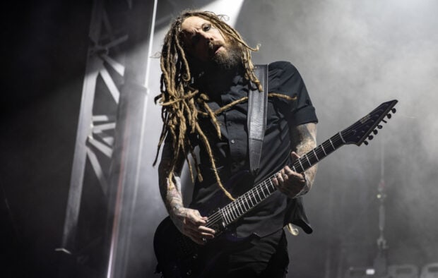 Korn guitarist with long dreadlocks playing an electric guitar on stage with fog in the background