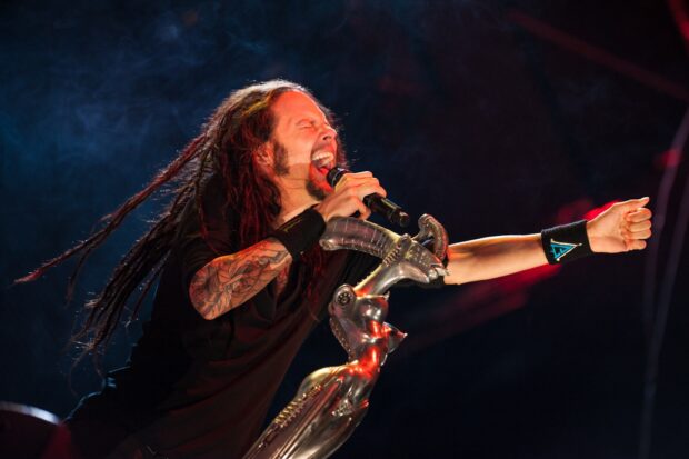 Korn lead singer performing energetically on stage with detailed microphone stand and visible tattoos