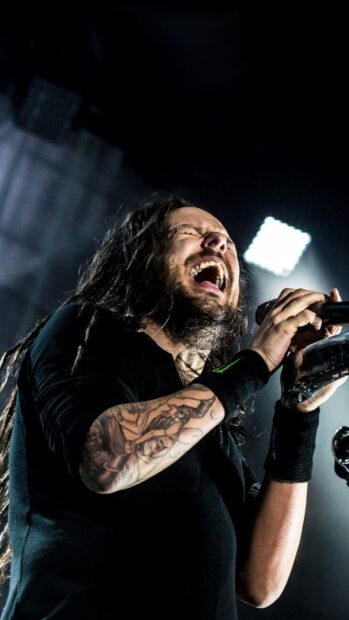 Korn vocalist performing passionately with tattooed arm on stage