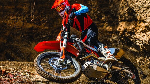 A rider in red gear maneuvers a KTM dirt bike through a rugged off road trail