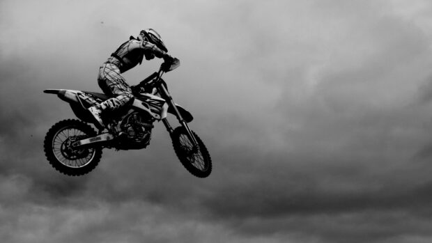 A rider in full gear jumps high on a KTM dirt bike against a cloudy sky background