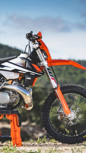Close up of an orange KTM dirt bike parked on rough terrain under a clear sky