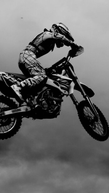 A rider in full gear jumps a KTM dirt bike against a cloudy sky in this high quality wallpaper