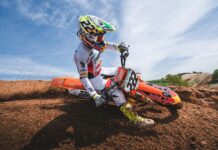 A KTM dirt bike rider wearing full gear powers through a dirt track on a bright day