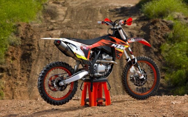 A high quality KTM dirt bike is displayed on a stand on a dirt track in this wallpaper