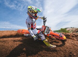 A KTM dirt bike rider wearing full gear powers through a dirt track on a bright day
